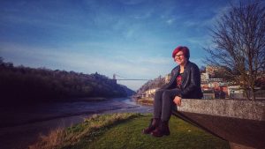 Image of a woman sitting on concrete overlooking River Avon with Suspension Bridge in the distance.