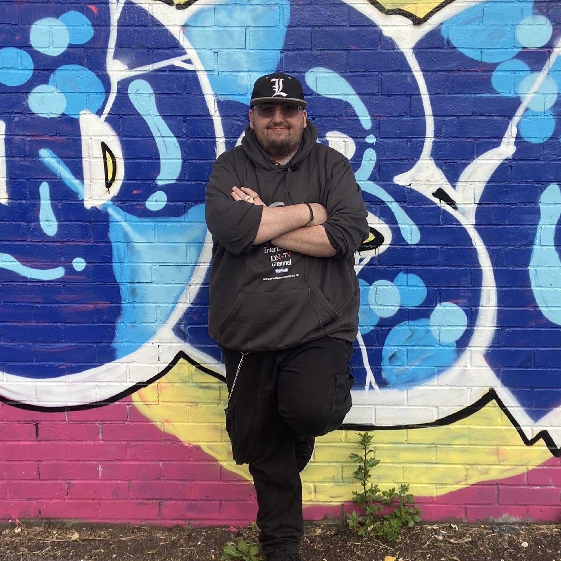 Drew standing arms crossed in front of a wall with colourful artwork on